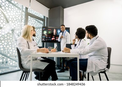 Medical Education And Training, Teamwork Concept. African Male Physician As A Speaker In Seminar, Having Lecture Or Report For His Multiracial Colleagues, Using Digital Screen And Schemes