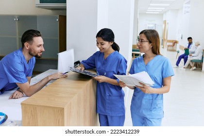 Medical employees. Medical assistant on duty talking with female nurses while working day in hospital standing near reception desk at lobby - Powered by Shutterstock