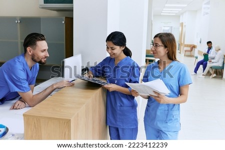 Medical employees. Medical assistant on duty talking with female nurses while working day in hospital standing near reception desk at lobby