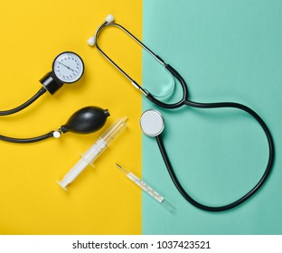 Medical equipment on a colored paper background. Stethoscope, syringe, thermometer, tonometer. Top view, flat lay.
