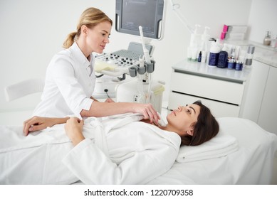 진찰. 갑상선 초음파 검사를 하는 백색 목욕 가운을 입은 아름다운 여인의 초상 스톡 사진