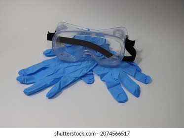 Medical Eye Protection Transparent Goggles With Blue Medical Gloves Isolated On A White Background. Health Care Worker Personal Protective Equipment. Selective Focus.