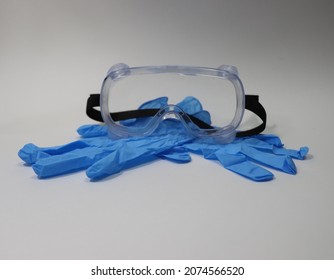 Medical Eye Protection Transparent Goggles With Blue Medical Gloves Isolated On A White Background. Health Care Worker Personal Protective Equipment. Selective Focus.