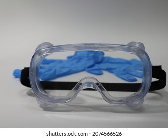 Medical Eye Protection Transparent Goggles With Blue Medical Gloves Isolated On A White Background. Health Care Worker Personal Protective Equipment. Selective Focus.