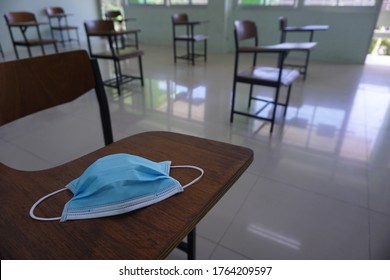 Medical Face Blue Mask On The Wood Lecture Chairs Place Distancing In The Empty Classroom. Concept During The Coronavirus Disease COVID-19 Outbreak In The 2020s. Back To School Concept.