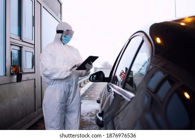 Medical Health Care Worker In Protective White Suit Controlling Passengers And PCR Test At Border Crossing Due To Global Corona Virus Pandemic.