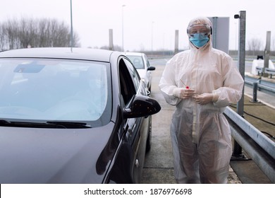 Medical Health Care Worker In Protective White Suit With Gloves Standing At Border Crossing And Holding Test Kit For Corona Virus.