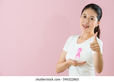 medical and health concept. healthy Chinese Asian model smile showing thumb up and hand under breast expressing fighting against cancer successful isolated on pink background. - Shutterstock ID 596322863