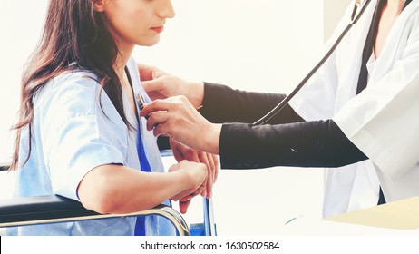 Medical Healthcare Concept.The Doctor Is Checking Female Patient Pulse.Health Check.The Doctor Uses Stethoscope To Listen To The Heart Rate Of Woman Patient In Wheelchair.