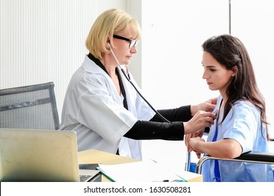 Medical Healthcare Concept.The Doctor Is Checking Female Patient Pulse.Health Check.The Doctor Uses Stethoscope To Listen To The Heart Rate Of Woman Patient In Wheelchair.