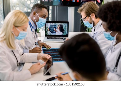 Medical And Healthcare Concept. Team Of Multiethnic Diverse Doctors Scientists, Wearing Face Masks, At Online Webinar With Young Experienced Afican Doctor, Counsulting About Results Of Patient CT