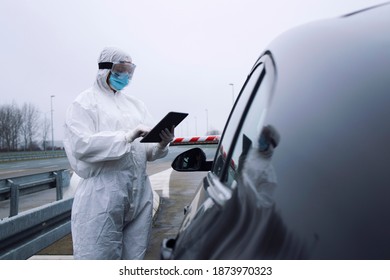 Medical Heath Care Worker In Protective White Suit Controlling Passengers And PCR Test At Border Crossing Due To Global Corona Virus Pandemic.