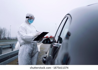 Medical Heath Care Worker In Protective White Suit Controlling Passengers And PCR Test At Border Crossing Due To Global Corona Virus Pandemic.