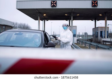 Medical Heath Care Worker In Protective White Suit Controlling Passengers And PCR Test At Border Crossing Due To Global Corona Virus Pandemic.