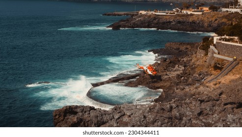 Medical helicopter landing on rocky volcanic shore for rescue operation at stormy ocean beach. Aviation provides first aid to the injured. - Powered by Shutterstock