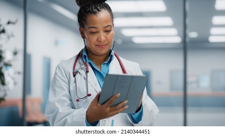 Medical Hospital Portrait: Confident African American Female Medical Doctor Using Digital Tablet Computer. Health Care Black Physician in White Lab Coat Prescribes Medicine, Ready to Save Lives - Powered by Shutterstock