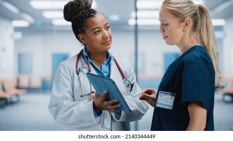 Medical Hospital: Professional Black Female Medical Doctor Talks With White Female Nurse Using Digital Tablet Computer. Two Health Care Specialists Discuss, Find Treatment Solution To Save Lives