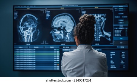 Medical Hospital Research Lab: Black Female Neuroscientist Looking At TV Screen, Analyzing Brain Scan MRI Images, Finding Treatment For Patient. Health Care Neurologist Curing People. Back View Zoom