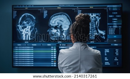 Medical Hospital Research Lab: Black Female Neuroscientist Looking at TV Screen, Analyzing Brain Scan MRI Images, Finding Treatment for Patient. Health Care Neurologist Curing People. Back View Zoom