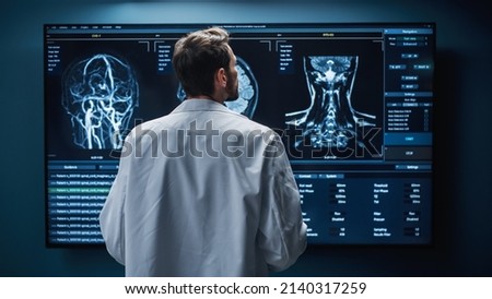 Medical Hospital Research Lab: White Male Neuroscientist Looking at TV Screen, Analyzing Brain Scan MRI Images, Finding Treatment for Patient. Health Care Neurologist Curing People. Back View Zoom