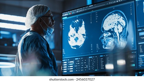 Medical Hospital Research Laboratory: Caucasian Male Neurosurgeon Looking At TV Screen With Brain MRI Scans Of Patient, Analyzing, Preparing For Complicated Neurosurgery, Wearing Surgical Gown. - Powered by Shutterstock