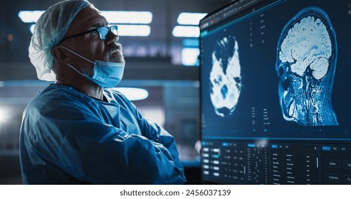 Medical Hospital Research Laboratory: Caucasian Male Neurosurgeon Looking At TV Screen With Brain MRI Scans Of Patient, Analyzing, Preparing For Complicated Neurosurgery, Wearing Surgical Gown. - Powered by Shutterstock