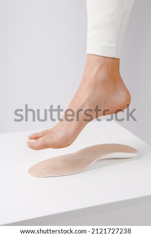 Medical insoles. Isolated orthopedic insoles on a white background. Treatment and prevention of flat feet and foot diseases. Foot care. Insole cutaway layers. Leg hanging over the insole.