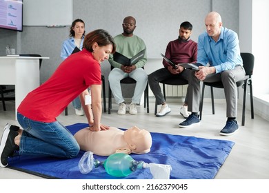 Medical instructor showing CPR on training mannequin on floor to people who sitting on chairs and watching during lesson - Powered by Shutterstock