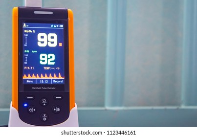 Medical Instrument, Handheld Pulse Oximeter  Used To Monitor Blood Oxygen In Patient In The Emergency Room At Hospital, Showing Normal Blood Oxygen Ninety-nine In Yellow And Pulse Ninety-two In Green.