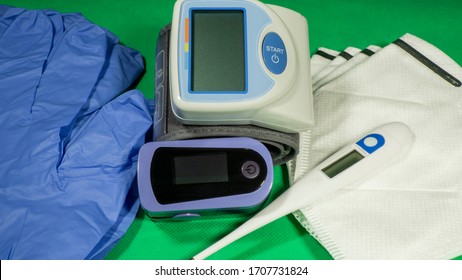 Medical Kit: Digital Body Thermometer, Pulse Oximeter, Medical Mask And Arm Blood Pressure Monitor. Disposable Medical Gloves. Kit To Check Values During Coronavirus Covid 19. Green Background