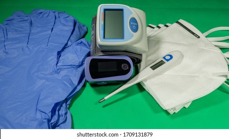 Medical Kit: Digital Body Thermometer, Pulse Oximeter, Medical Mask And Arm Blood Pressure Monitor. Disposable Medical Gloves. Kit To Check Values During Coronavirus Covid 19. Green Background