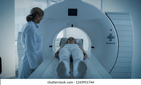 In Medical Laboratory Female Radiologist Controls MRI Or CT Or PET Scan With Female Patient Undergoing Procedure. Doctor Conducts Emergency Scanning With Advanced Medical Technologies. In Blue Tone.