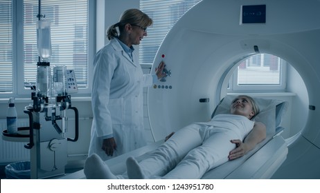 In Medical Laboratory Female Radiologist Controls MRI Or CT Or PET Scan With Female Patient Undergoing Procedure. Doctor Conducts Emergency Scanning With Advanced Medical Technologies. In Blue Tone.