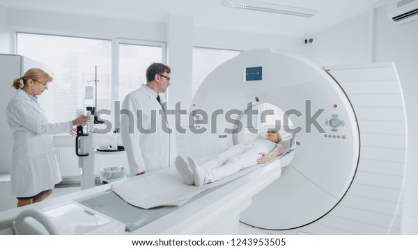 In Medical Laboratory\
Female Radiologist and Male Doctor Control and Monitor MRI or CT\
Scan with Female Patient Undergoing Procedure. High-Tech Modern\
Medical Equipment.