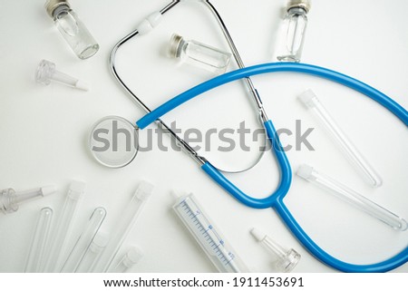 Medical layout on white background, flat lay. Blue stethoscope or phonendoscope surrounded by vials, ampoules and test tubes.