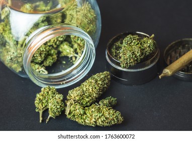 Medical Marijuana flower buds in glass jar and grinder on dark backdrop