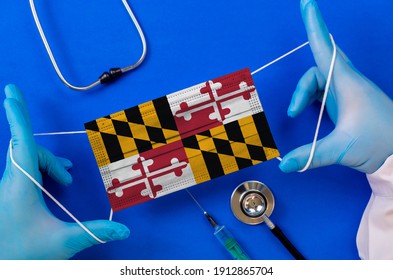 Medical Mask With The Flag Of Maryland In The Hands Of A Doctor And Stethoscope, Flat Lay. Coronavirus Pandemic