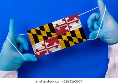 Medical Mask With The Flag Of Maryland In The Hands Of A Doctor, Flat Lay. Coronavirus Infection COVID-19