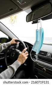 Medical Mask Hanging On Rear View Mirror In Car Of Female Driver