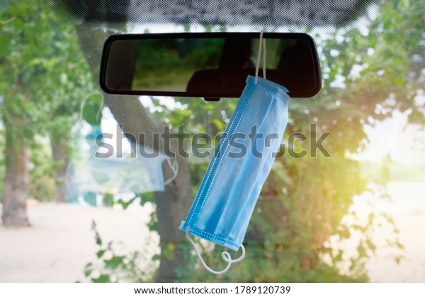 A medical mask hangs on the car\
mirror in the passenger compartment. Protective mask to protect\
against viruses while driving. Coronavirus,\
Pandemic