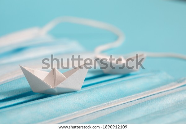 Medical mask as metaphor for the sea.  Paper ship\
sails on background. Concept of protection of tourism in the age of\
kovid 19