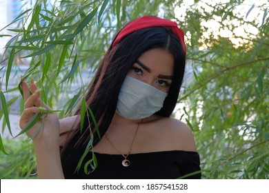 Medical mask on an Asian girl. Covid epidemic time. Asian woman wear a face mask while posing in the park against willow branches, vintage color. Aspirine first time was extracted from willow bark