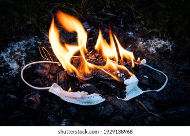 Medizinische Maske auf schwarzem Hintergrund mit der Aufschrift covid-19. Vernichtung der Schutzmaske durch Verbrennung. Verschmutzung der Natur durch Covid-Masken. Das Koronavirus wird in einem Feuer zerstört.