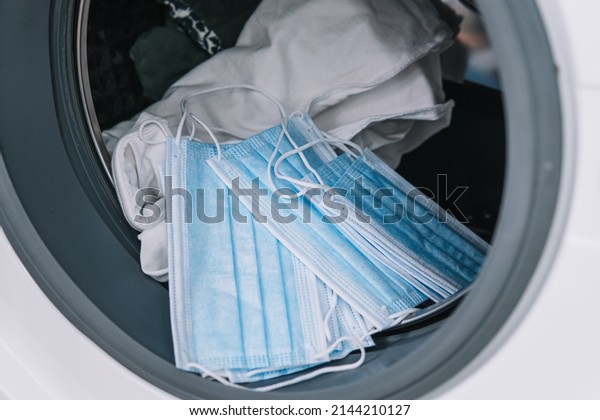 Medical masks and dirty clothes in washing\
machine. Washing machine\
loading