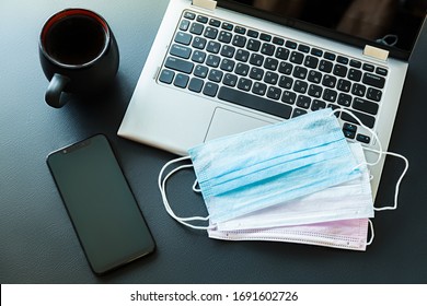 Medical masks on a laptop with a smartphone, antibacterial wipes and a cup of coffee on a black background. Quarantine workplace at home concept. Coronavirus covid-19