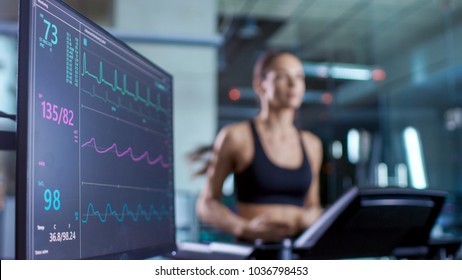 Medical Monitor Shows EKG Reading Of A Woman Athlete Running On A Treadmill. Focus On Monitor.