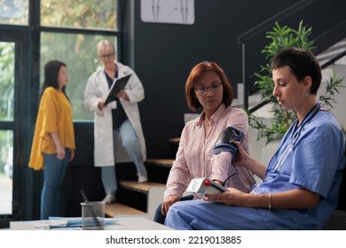 Medical Nurse Doing Cardiology Exam With Instrument To Measure Hypertension And Hypotension, Checking Blood Pressure With Tonometer. Assisatnt Measuring High Or Low Pulse, Consultation With Patient