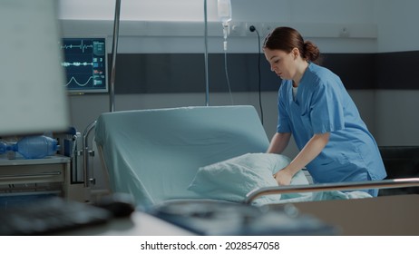 Medical Nurse Preparing Hospital Ward Bed With Pillow And Blanket For Comfort Of Sick Person. Intensive Care Unit Filled With Modern Medical Equipment For Disease Treatment, Surgery Recovery