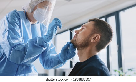 Medical Nurse in Safety Gloves and Mask, Protective Face Shield and Overalls is Taking a PCR Corona Virus Sample in a Health Clinic. Doctor Uses Respiratory Swab Test. Covid-19 Pandemic Concept.
