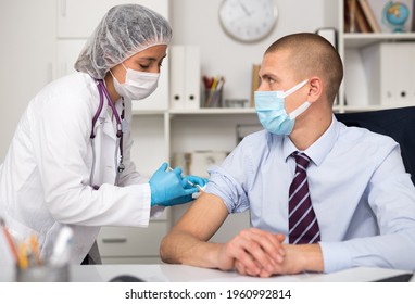 Medical Nurse In Safety Gloves And Protective Mask Making Vaccine Injection To A Patient In Health Clinic